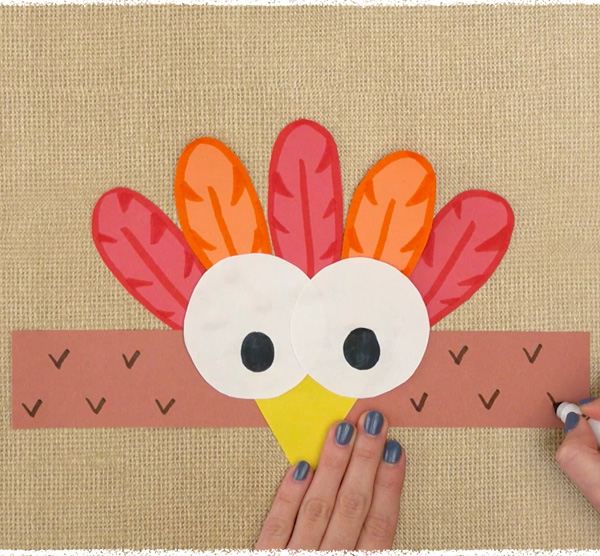 Hands creating a turkey headband craft on light brown textured background