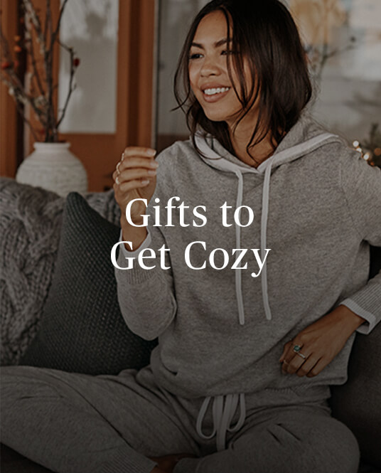 Gifts to Get Cozy copy over an image of a brunette woman sitting in the Summersalt Coziest Cashmere Blend Hoodie in Wolf
