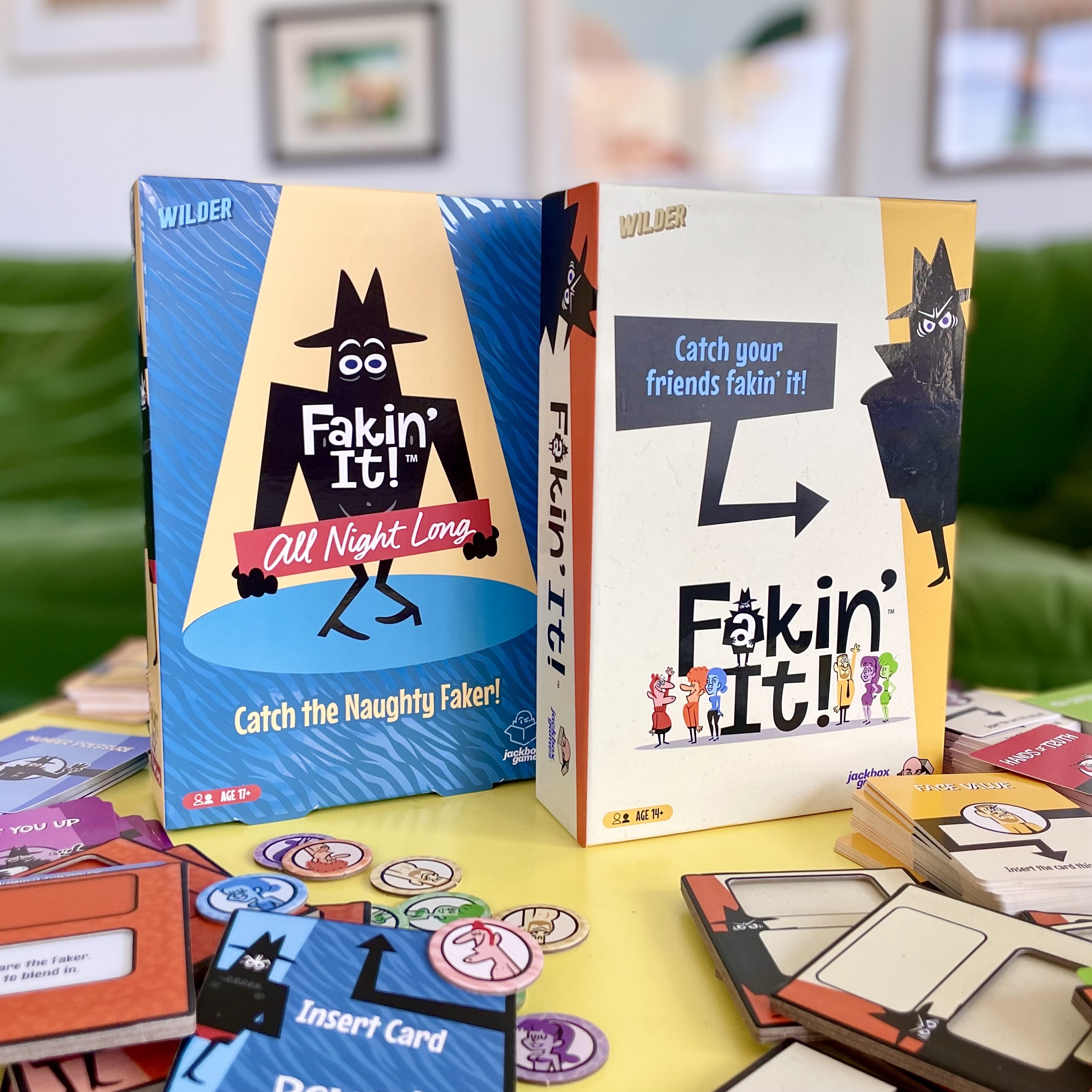 Photos of the Fakin' It and Fakin' It All Night Long board game boxes on a living room table surrounded by the game cards