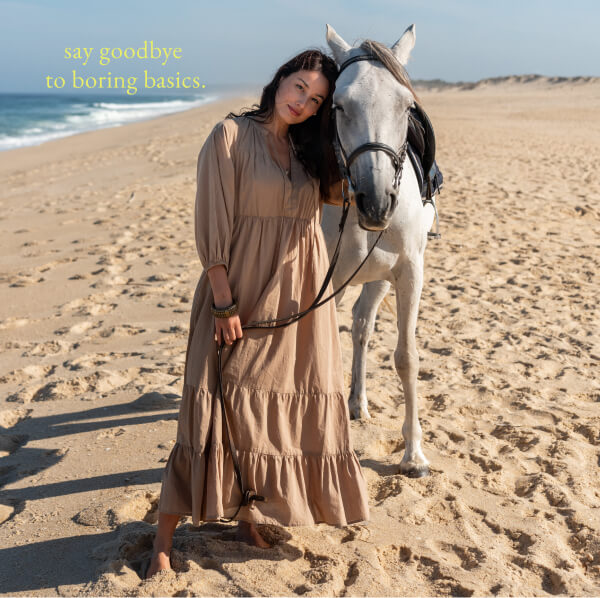 Say goodbye to boring basics. - Image of a woman in a brown long sleeve tiered maxi dress on a beach with a horse