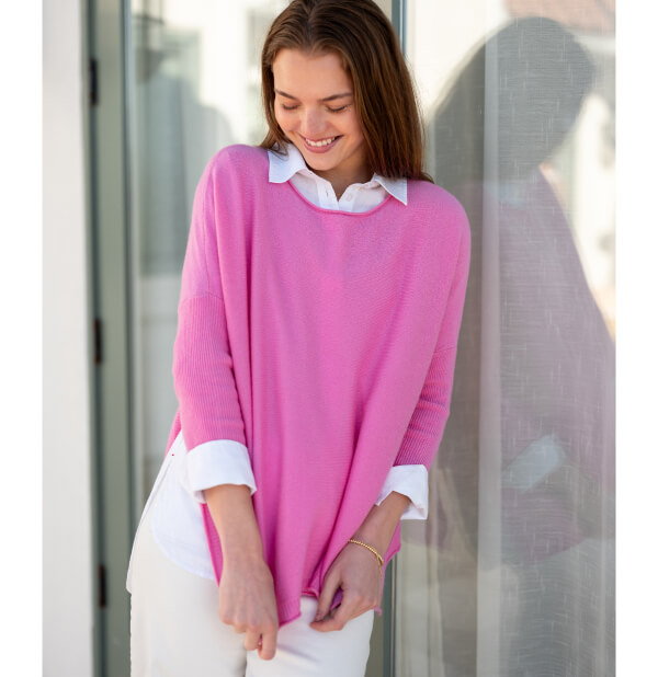 Image of a woman wearing a pink cashmere sweater with rolled hems and side slits.