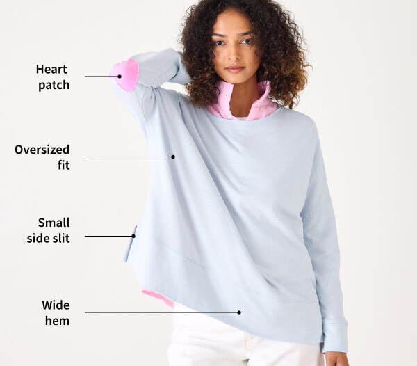 Image of a woman wearing a light blue long sleeve tee with pink heart patches on the elbows with the details called out