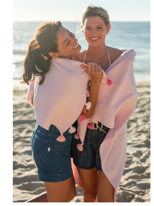 Image of two women on a beach wearing a pink wrap with pink tassles