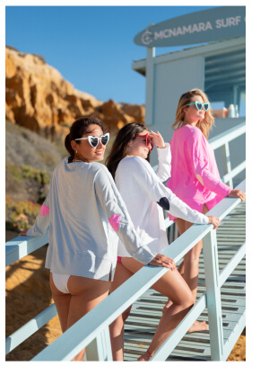 Image of three women on a beach wearing different color long sleeve tees with heart patches on the elbows