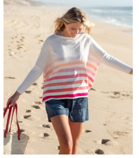 Image of a woman walking on a beach wearing a white sweater with ombre pink stripes