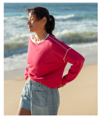 Image of a woman on the beach wearing a pink sweater with white trim