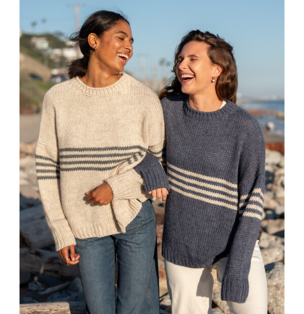 image of two women on the beach wearing a white sweater and blue sweater