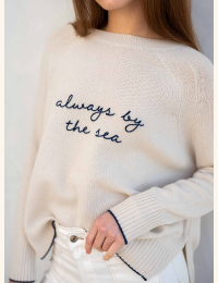 Image of a woman in a cream cashmere sweater that says "always by the sea"