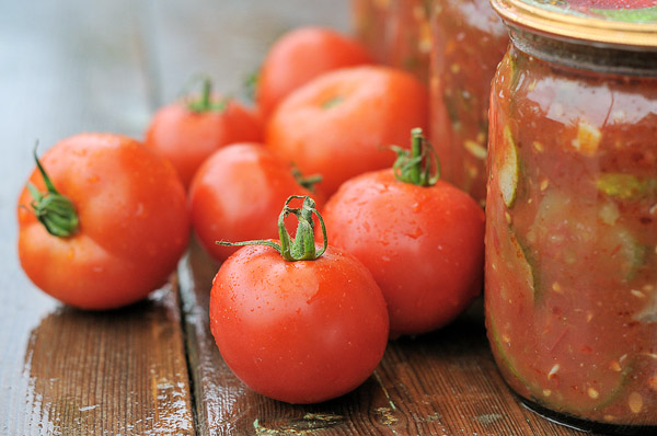 Ripe tomatoes next to jars of tomato sauce