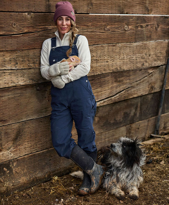 Woman holding a piglet with a dog