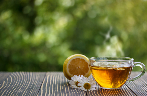 Half a lemon, a glass teacup with a teabag steeping, and a couple daisies