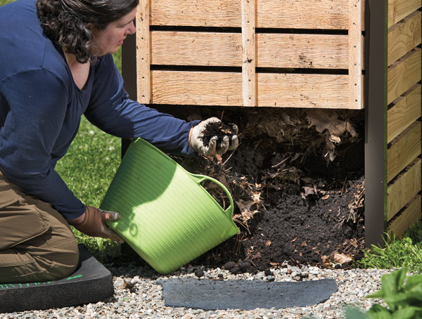 Image of woman pulling finished compost from the bottom of a cedar composter.