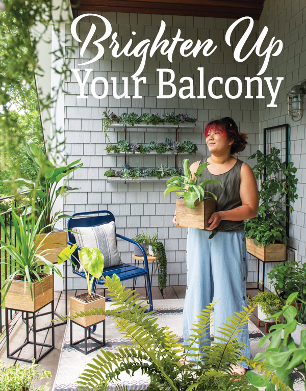 Brighten Up Your Balcony. Pictured; Young woman standing on her balcony, holding a Tartu Planter with a houseplant. Balcony is filled with planter tables full of houseplants and a blue chair in the corner.