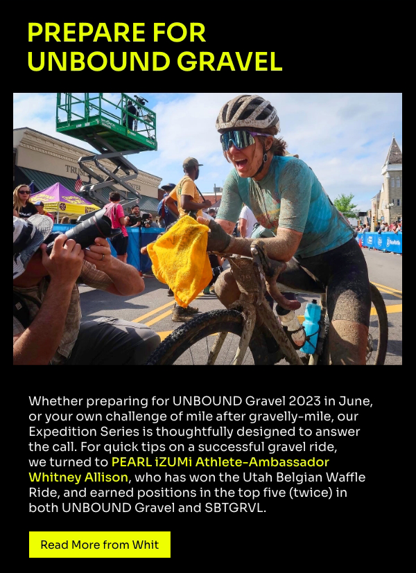 Whit Allison at the finish line of Unbound Gravel, covered in mud and surrounded by photographers