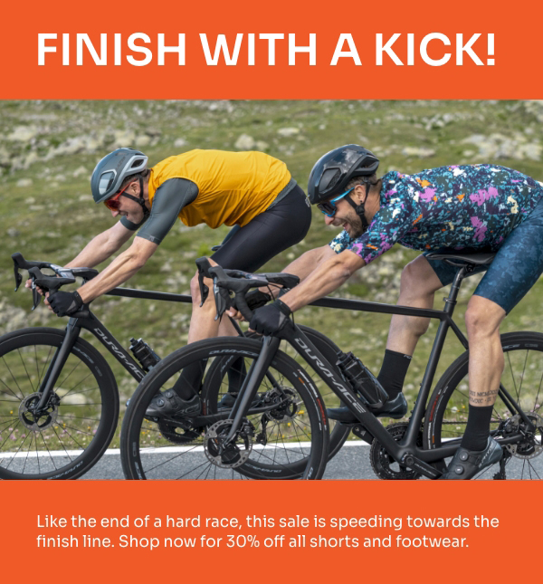 Two male cyclists push their bikes over the finish line