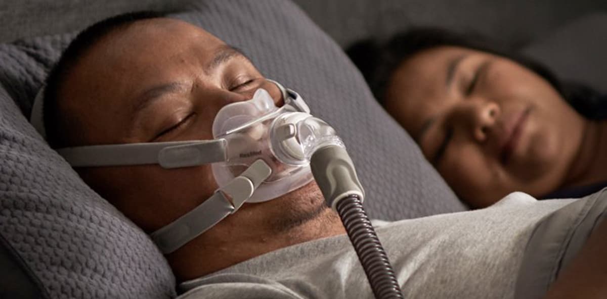 Couple lying in bed asleep. Man is using a CPAP mask.