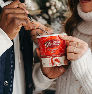 Two People Holding Peppermint Stick Ice Cream in front of a Christmas Tree